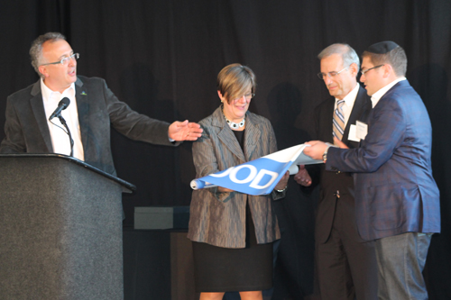 Lev Gonick, Shaker Heights Mayor   Earl Leiken, outgoing OneCommunity board chair Dorothy Baunach and Sam Krichevsky, COO of LaunchHouse unfurled a banner